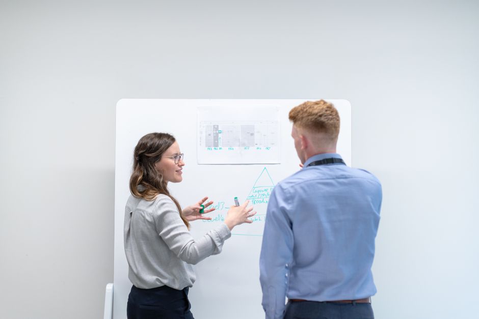 Two professionals discussing project plans at whiteboard in office setting.