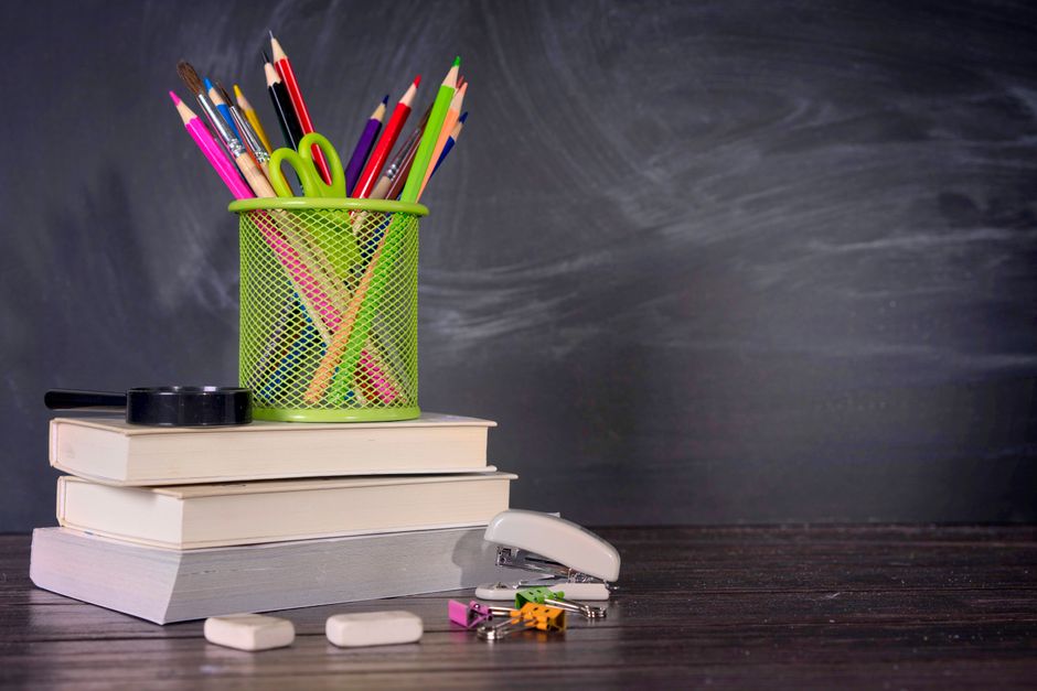 A collection of school stationery including pencils and books against a blackboard. Ideal for educational themes.